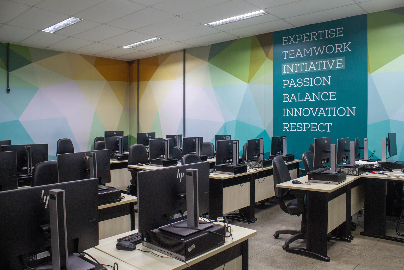 Laboratório de informática com fileiras de computadores e uma parede com padrão geométrico colorido